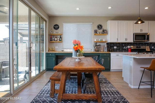 kitchen with appliances with stainless steel finishes, decorative light fixtures, white cabinets, decorative backsplash, and light hardwood / wood-style floors