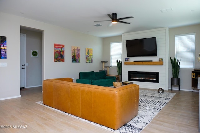 living room featuring ceiling fan, a large fireplace, and light hardwood / wood-style flooring