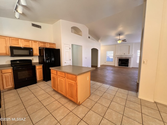 kitchen featuring light tile patterned floors, ceiling fan, a center island, a fireplace, and black appliances