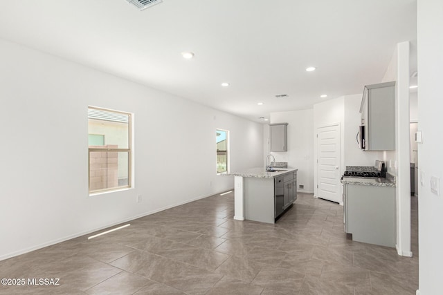 kitchen with sink, gray cabinets, an island with sink, and light stone countertops