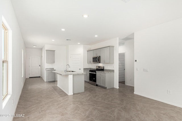 kitchen featuring sink, a kitchen island with sink, gray cabinetry, stainless steel appliances, and light stone countertops