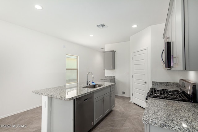 kitchen featuring appliances with stainless steel finishes, light stone countertops, and an island with sink