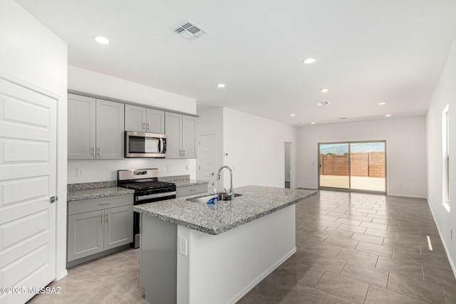 kitchen with an island with sink, appliances with stainless steel finishes, sink, and gray cabinetry