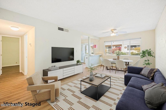 living room with ceiling fan, a textured ceiling, and light hardwood / wood-style flooring