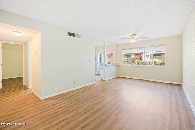 unfurnished living room featuring brick wall, a textured ceiling, ceiling fan, and light hardwood / wood-style flooring