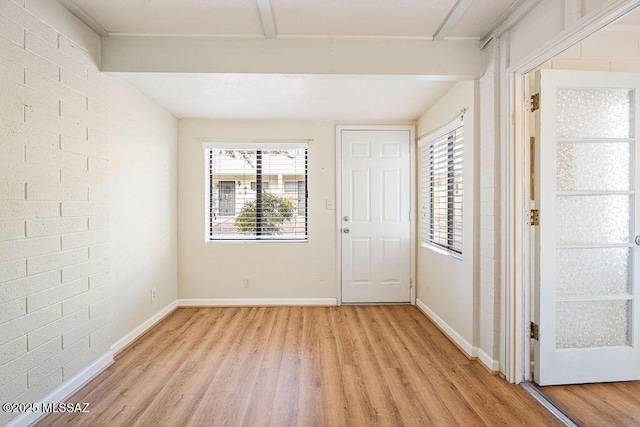 foyer entrance with brick wall, plenty of natural light, beam ceiling, and light hardwood / wood-style flooring