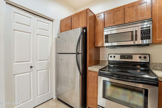 kitchen with light stone counters, stainless steel appliances, and light tile patterned flooring