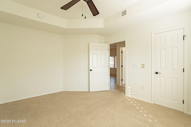 spare room featuring light carpet, a tray ceiling, and ceiling fan