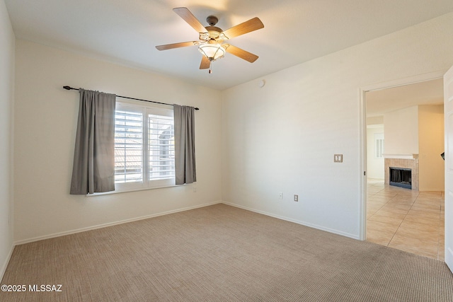 carpeted spare room featuring a tile fireplace and ceiling fan