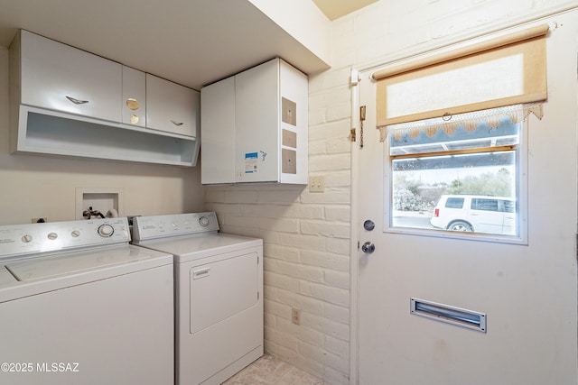 clothes washing area featuring cabinets, brick wall, and washing machine and clothes dryer