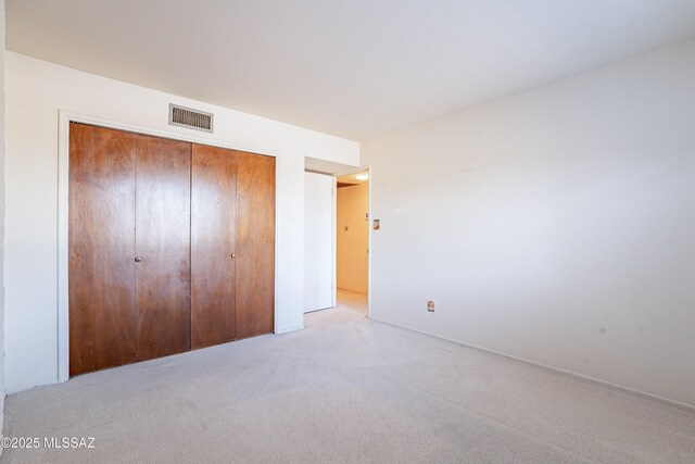 unfurnished bedroom featuring light carpet, visible vents, and a closet