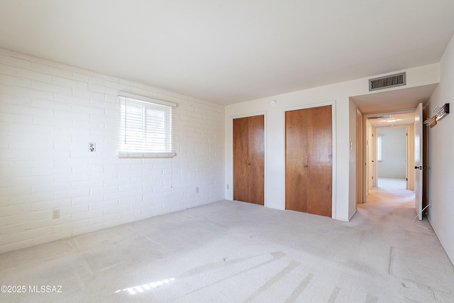 unfurnished bedroom featuring multiple closets, light colored carpet, visible vents, and brick wall