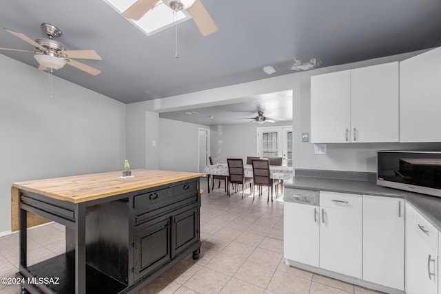 kitchen with wood counters, white cabinetry, a skylight, light tile patterned floors, and ceiling fan