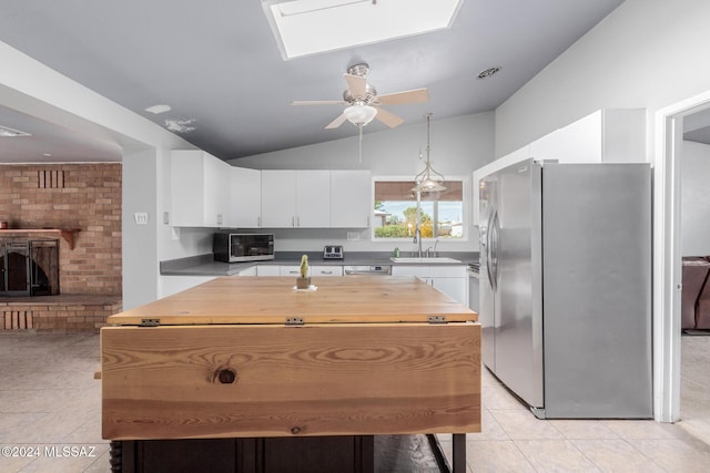 kitchen with sink, appliances with stainless steel finishes, lofted ceiling with skylight, a fireplace, and white cabinets