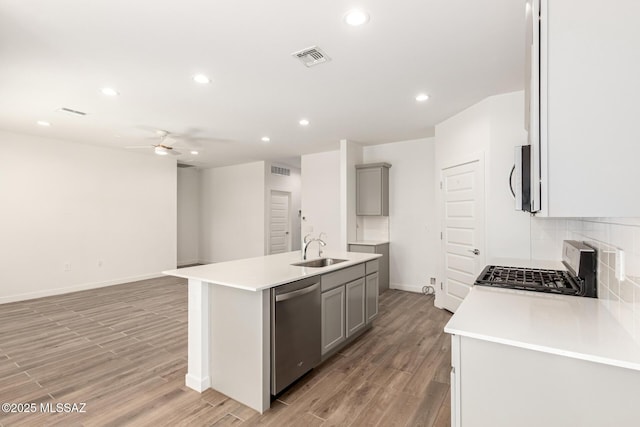 kitchen featuring gray cabinetry, stainless steel appliances, a sink, open floor plan, and decorative backsplash