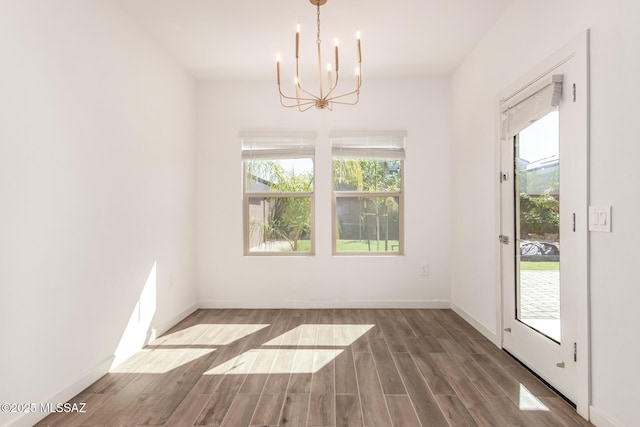 unfurnished dining area featuring an inviting chandelier, baseboards, and wood finished floors