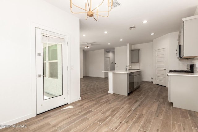 kitchen with light wood finished floors, backsplash, appliances with stainless steel finishes, open floor plan, and a kitchen island with sink