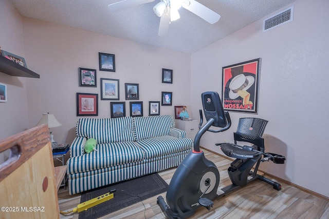 exercise room featuring wood-type flooring, ceiling fan, and a textured ceiling