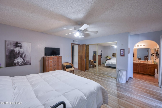 bedroom featuring ceiling fan, ensuite bath, a closet, and a textured ceiling