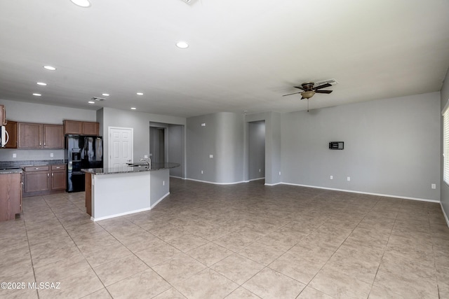 kitchen featuring sink, dark stone counters, a kitchen island with sink, ceiling fan, and black fridge with ice dispenser