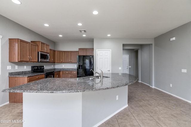 kitchen with a large island with sink, stone countertops, sink, and black appliances