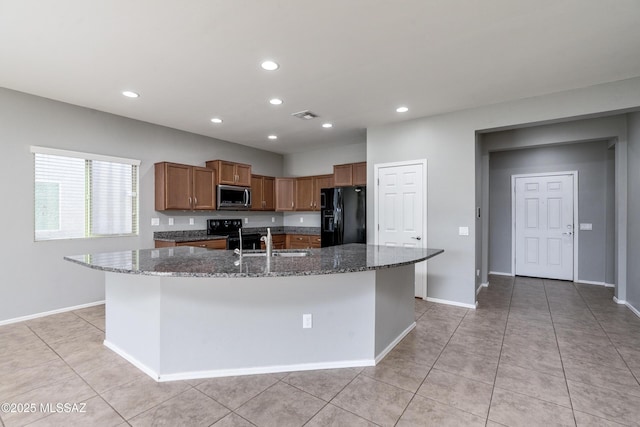 kitchen featuring light tile patterned flooring, sink, dark stone countertops, an island with sink, and black appliances