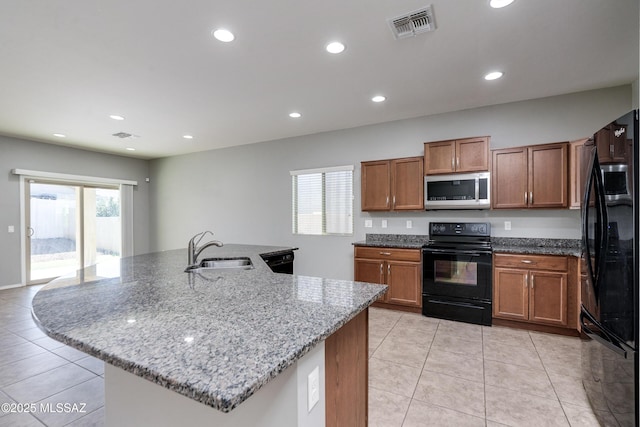 kitchen with a kitchen island with sink, sink, light stone counters, and black appliances