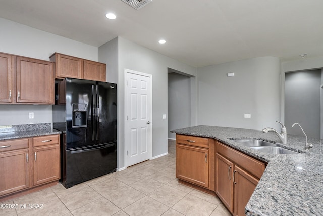 kitchen featuring light stone countertops, sink, light tile patterned floors, and black fridge with ice dispenser