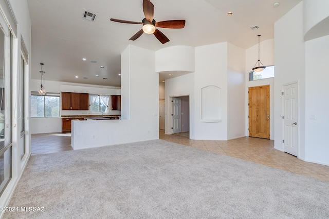 unfurnished living room featuring ceiling fan, light colored carpet, and a high ceiling