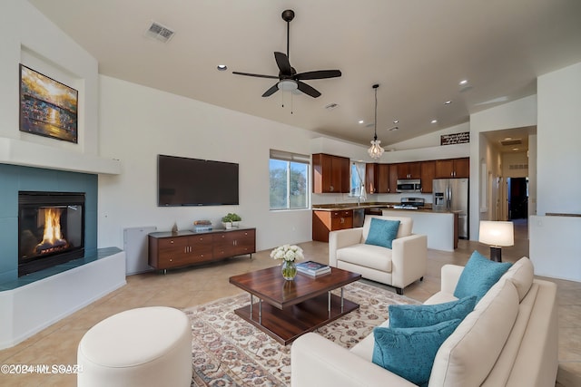 living room with light tile patterned floors, sink, ceiling fan, a tiled fireplace, and vaulted ceiling