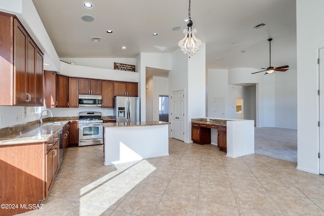 kitchen featuring sink, appliances with stainless steel finishes, light stone countertops, a kitchen island, and decorative light fixtures