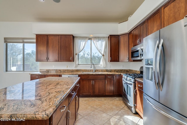 kitchen featuring sink, light stone counters, a center island, light tile patterned floors, and stainless steel appliances