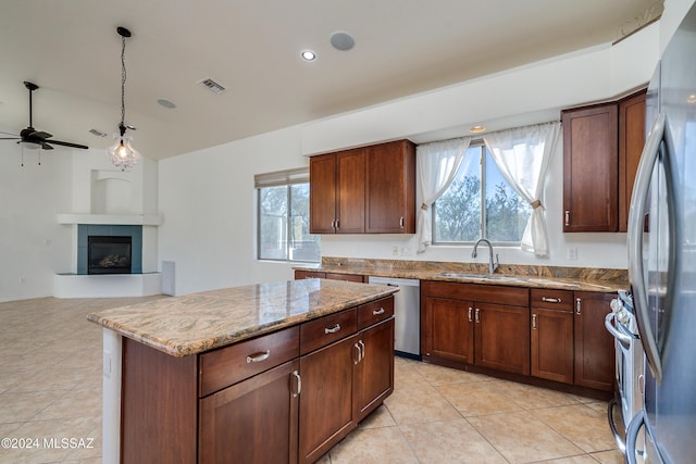 kitchen with appliances with stainless steel finishes, sink, hanging light fixtures, a tiled fireplace, and light stone counters