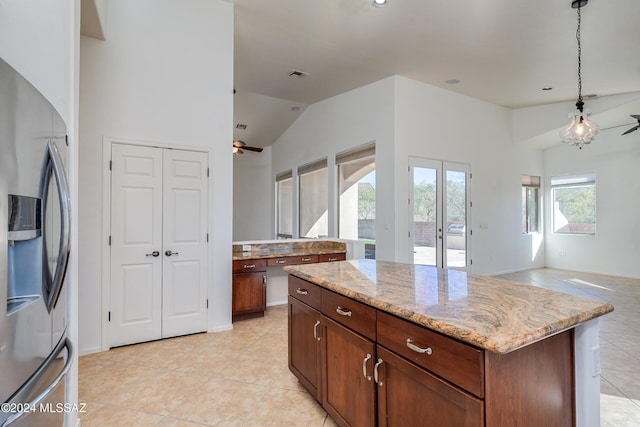 kitchen featuring light stone counters, a kitchen island, stainless steel fridge with ice dispenser, decorative light fixtures, and vaulted ceiling