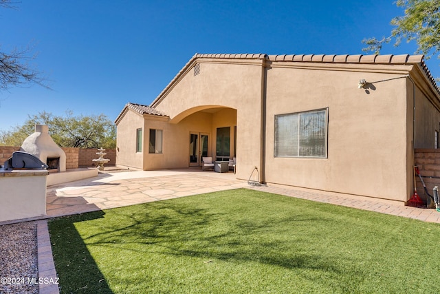 back of property with a patio, a yard, and exterior fireplace