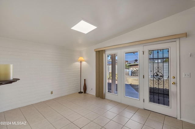 doorway to outside featuring light tile patterned flooring, brick wall, vaulted ceiling, and french doors