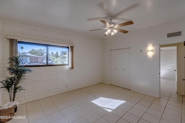 tiled empty room with ceiling fan and brick wall