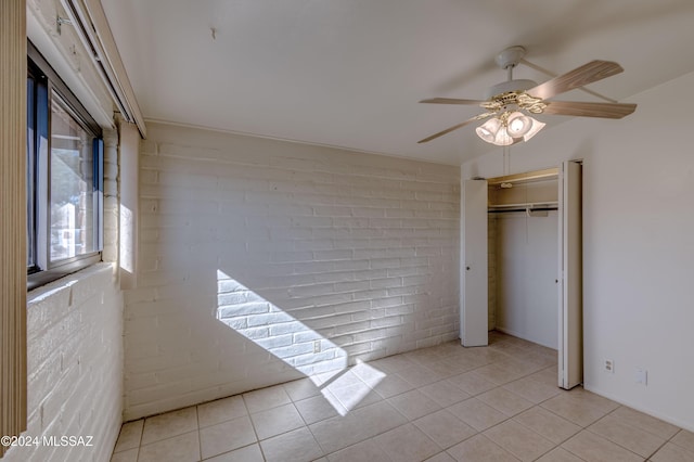 unfurnished bedroom with ceiling fan, brick wall, a closet, and light tile patterned floors