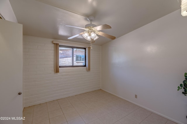 tiled spare room featuring ceiling fan and brick wall