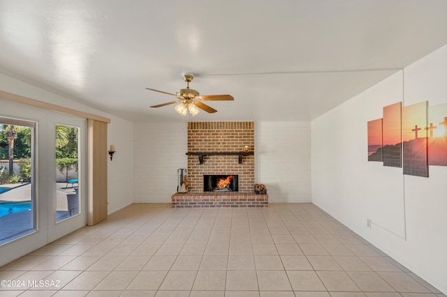 unfurnished living room with light tile patterned floors, a fireplace, ceiling fan, and brick wall