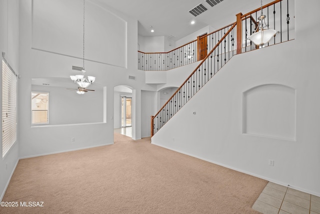 unfurnished living room with ceiling fan, light carpet, and a high ceiling
