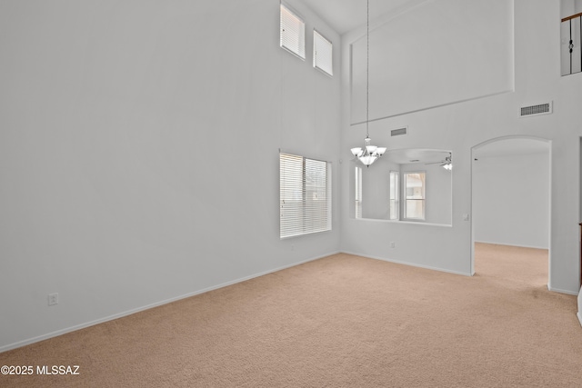 interior space featuring ceiling fan with notable chandelier, light colored carpet, a healthy amount of sunlight, and a towering ceiling