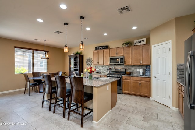 kitchen featuring a breakfast bar, light stone counters, decorative light fixtures, stainless steel appliances, and a kitchen island with sink