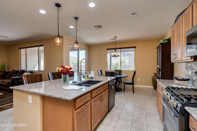 kitchen with sink, appliances with stainless steel finishes, an island with sink, pendant lighting, and light stone countertops