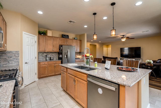 kitchen with sink, appliances with stainless steel finishes, an island with sink, pendant lighting, and light stone countertops