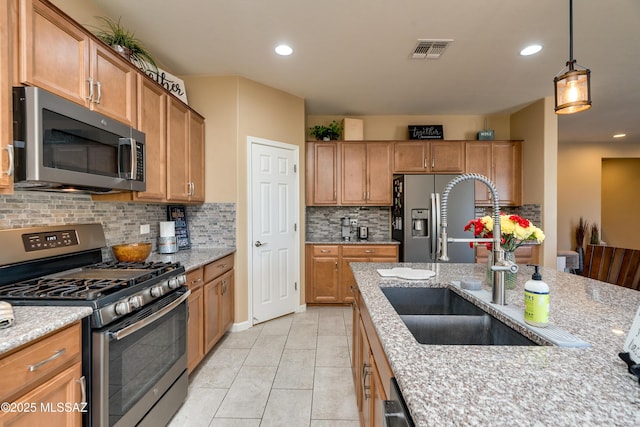 kitchen featuring light stone counters, sink, stainless steel appliances, and hanging light fixtures