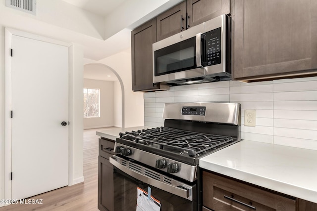 kitchen featuring dark brown cabinetry, stainless steel appliances, light hardwood / wood-style floors, and decorative backsplash