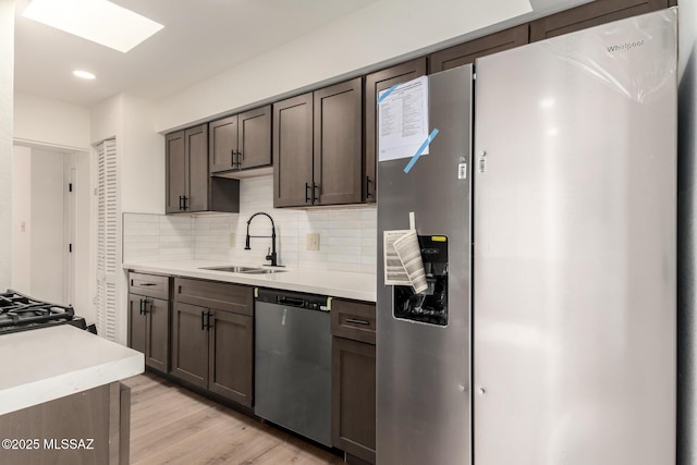 kitchen with appliances with stainless steel finishes, sink, decorative backsplash, dark brown cabinets, and light wood-type flooring