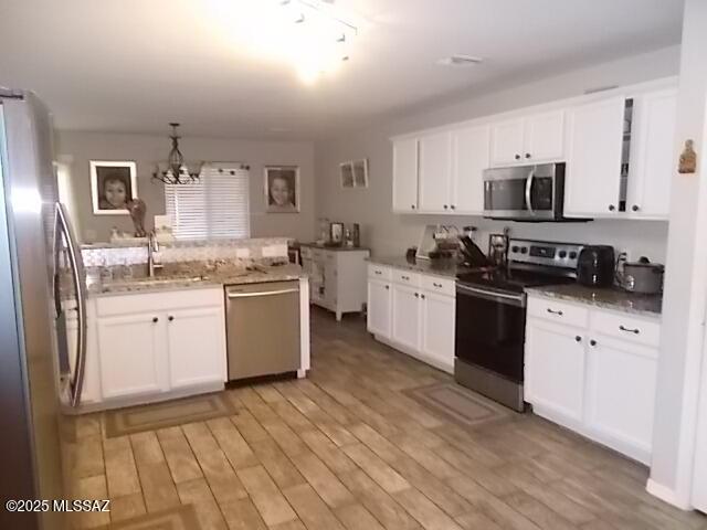 kitchen featuring sink, hanging light fixtures, light wood-type flooring, appliances with stainless steel finishes, and white cabinets