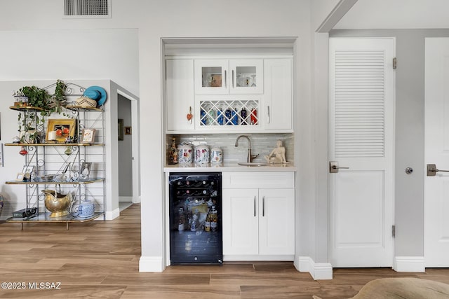 bar with sink, white cabinetry, hardwood / wood-style floors, decorative backsplash, and beverage cooler